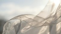Flowing translucent fabric with soft golden light creating elegant waves and shadows against neutral background for luxury design projects.