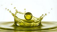 Olive oil or golden liquid splashing with droplets and sphere on white background, isolated for culinary, cosmetic, and wellness design applications.