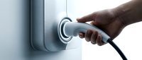 Hand plugging electric vehicle charging connector into a wall-mounted EV charger station, sustainable green energy concept.