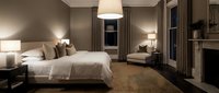 Luxurious master bedroom with neutral tones, upholstered bed, pendant lighting, fireplace, and elegant furnishings for interior design and hospitality projects.