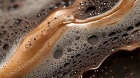Creamy brown coffee foam with bubbles and swirls creating abstract patterns on dark background, macro photography showing rich texture and movement.