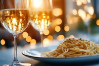 Elegant pasta dinner with white wine glass on table with warm golden bokeh lights creating romantic dining atmosphere for restaurant menu design.