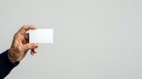 Hand holding blank white business card against neutral background, suitable for branding, corporate identity, and marketing mockup presentations.