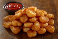 Golden crispy potato tots piled on wooden surface with small bowl of ketchup, perfect for appetizer menus or comfort food photography.
