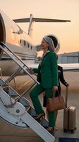Professional businesswoman in green suit boarding private jet at sunset with luggage for luxury corporate travel and executive lifestyle.