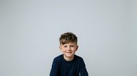Young boy with light brown hair and fair complexion wearing dark navy t-shirt, smiling at camera against neutral gray background. Studio portrait suitable for family, education, healthcare and lifestyle marketing materials.