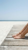 Woman's bare feet resting on wooden boardwalk extending toward calm ocean and sandy beach on clear day. Relaxation and vacation concept for travel and leisure marketing.