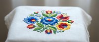 Traditional folk embroidery with colorful floral motif on white fabric featuring blue and red flowers with green leaves for textile design projects.