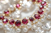 Elegant jewelry macro with red rubies and white pearls on golden setting, sparkling diamonds create luxurious pattern against soft bokeh background.