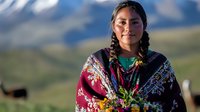Young Indigenous woman in traditional colorful clothing smiling outdoors with mountain landscape background, cultural heritage and ethnic diversity concept.