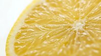 Fresh lemon slice macro shot showing juicy yellow citrus texture, vibrant pulp detail on white background for food and health design.