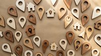 Wooden location pins and house icons scattered on kraft paper background for real estate, navigation and property business concepts.