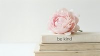 Soft pink peony resting on stacked books with be kind text, pastel minimalist lifestyle flat lay for wellness and inspiration.