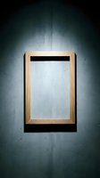 Empty wooden frame hanging on a dark concrete wall with dramatic spotlight lighting, creating a moody gallery atmosphere for art display mockups.
