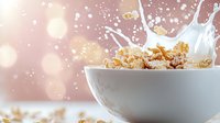 Crunchy cereal flakes splashing in white milk bowl with dynamic motion and bokeh light effect on pink background. Breakfast food photography.