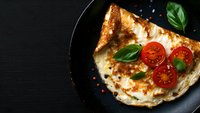 Homemade calzone with melted mozzarella, fresh cherry tomatoes and basil leaves on black plate against dark background, copy space for menu design.
