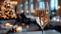 Glass of sparkling rose wine with blurred festive lights and candles in background creating romantic holiday atmosphere for celebration or date night.