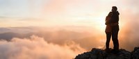 Silhouette of hiker standing on mountain peak above clouds during golden sunrise, adventure travel and outdoor exploration concept for motivational content.