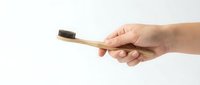 Hand holding a bamboo toothbrush with charcoal bristles on white background, eco-friendly oral care concept for dental and sustainability.