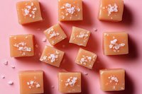 Salted caramel candy squares topped with pink sea salt crystals arranged on pink background, sweet and salty dessert confection pattern layout.