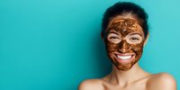 Young woman with chocolate facial mask smiling against turquoise background. Skincare and beauty treatment concept for spa and wellness advertising.