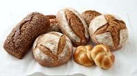 Assorted fresh baked bread loaves and rolls including whole wheat, sourdough, and artisan varieties on white background for bakery, food, and culinary use.