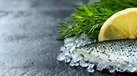 Fresh raw fish fillet with sea salt crystals and lemon slice on gray stone surface, suitable for culinary, food styling, restaurant menus, and cooking content.