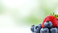 Fresh organic strawberry and blueberries on soft green background for healthy eating and nutrition concepts.