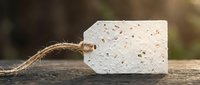 Blank white kraft paper tag with twine attached, isolated on wooden surface for product labeling, gift wrapping, and retail branding applications.