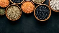 Assorted legumes and pulses in wooden bowls on dark surface, including lentils, beans, and chickpeas for cooking and nutrition.