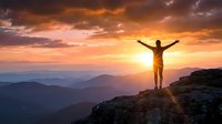 Person with raised arms celebrating success on mountain peak at golden sunrise with dramatic sky and layered mountain ranges creating inspirational achievement moment.