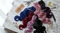 Colorful wavy hair extensions in blue, burgundy, pink and black arranged on marble surface with styling tools, wooden comb, scissors and hair clips for salon or beauty design projects.