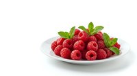 Fresh red raspberries with green leaves arranged on white plate, isolated on white background. Suitable for food, nutrition, healthy eating, recipe, and culinary design projects.