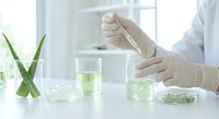 Laboratory scientist in white coat and gloves conducting plant research with green leaf extracts in glass beakers for natural cosmetics development.