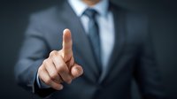 Businessman in formal suit pointing finger forward against dark background, representing leadership, choice, or digital interface interaction.