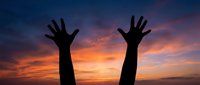 Silhouette of human hands raised up against dramatic sunset sky with orange and purple clouds expressing freedom, victory, celebration, and spiritual connection.