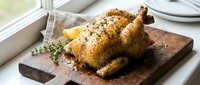 Golden roasted whole chicken with herbs and spices on wooden cutting board, ready to serve for family dinner or holiday meal preparation in kitchen.