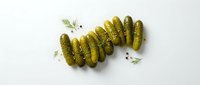 Pickled gherkins arranged in a row on white background with fresh dill sprigs and scattered peppercorns, suitable for food packaging and culinary content.