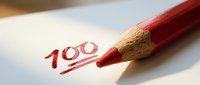 Red pencil marking 100 percent score on white paper with underline, academic achievement and perfect test results for educational success.