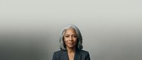 Mature woman with gray hair wearing dark blazer against neutral gradient background, suitable for corporate, business, and professional website design.