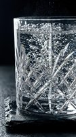 Crystal whiskey glass filled with sparkling water and rising bubbles on dark slate surface, close-up studio shot on black background.