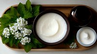 Fresh hawthorn flowers with green leaves alongside ceramic bowls containing white cream and dark syrup on wooden serving tray, natural skincare concept.