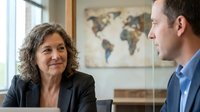 Professional middle-aged Hispanic businesswoman with curly hair in black blazer having meeting with Caucasian male colleague in modern office setting.