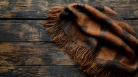 Cozy brown plaid wool scarf with fringe lying on dark rustic wooden background. Natural winter accessory photographed from above with dramatic lighting.