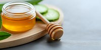 Fresh honey in glass jar with wooden dipper on bamboo board, cucumber slices and green leaves. Natural organic sweetener for healthy lifestyle.