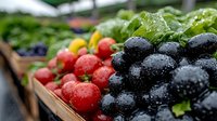 Fresh berries with water droplets at farmers market - ripe blackberries, strawberries, and yellow raspberries in wooden crates with green leafy vegetables in background.