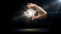 Hands protecting glowing star symbol with bright light rays on dark background representing success, achievement, excellence and business goals.