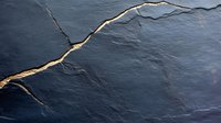Dark gray stone or slate texture with golden crack pattern running diagonally, representing kintsugi art concept or geological formations. Natural luxury background.