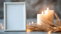 Empty white photo frame with glowing candles and dried pampas grass on blurred background with bokeh lights creating cozy atmospheric composition.