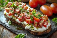 Fresh bruschetta with cherry tomatoes, creamy ricotta cheese, and chopped basil on rustic bread, served on dark stone plate with herbs and olive oil drizzle.